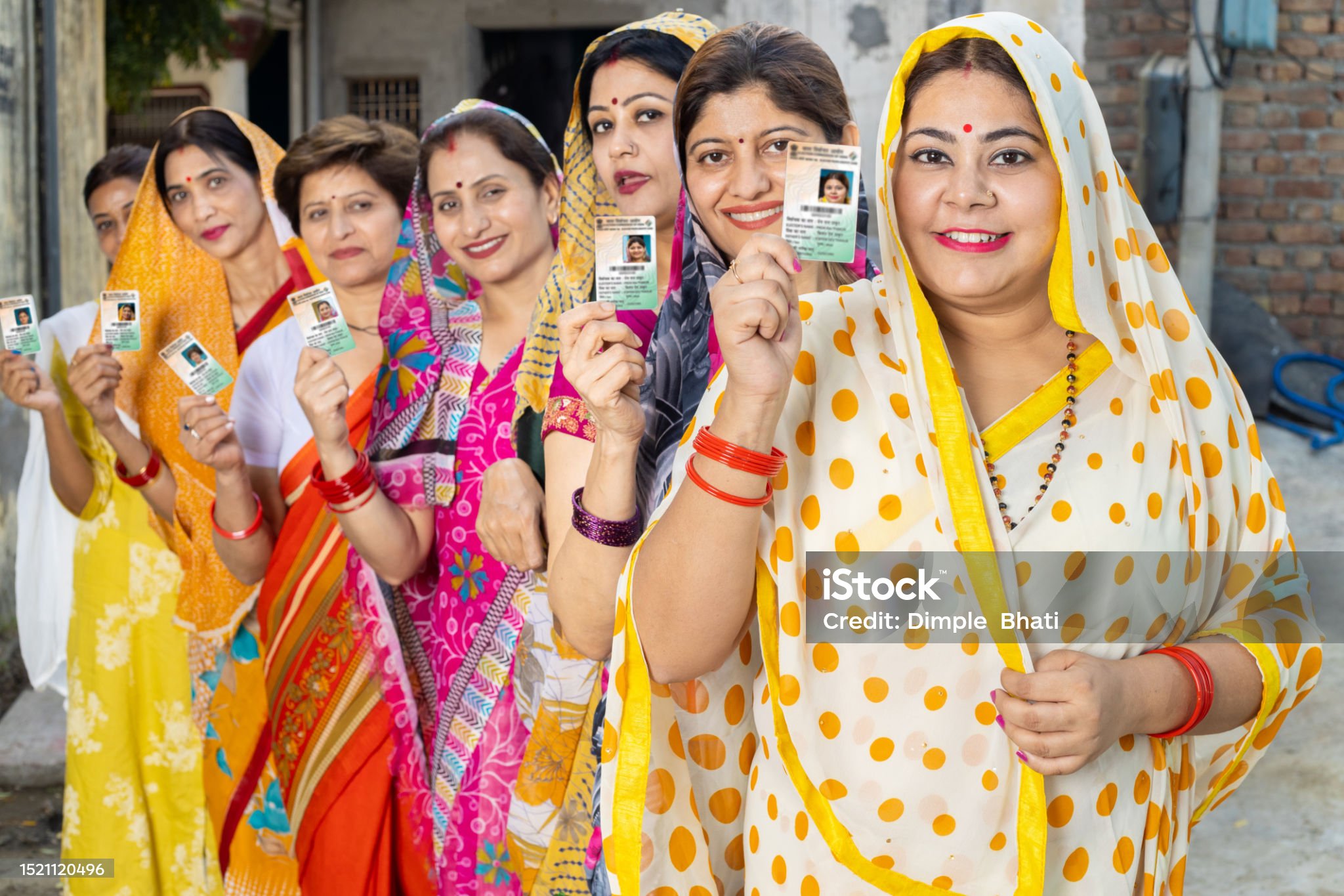 बिहार विधानसभा चुनाव 2025एक कतार में खड़ी भारतीय महिलाएँ रंगीन साड़ियों में पहने हुए अपने वोटर पहचान पत्र दिखा रही हैं, जो बिहार चुनाव के दौरान मतदान केंद्र के बाहर मतदान का इंतजार कर रही हैं।